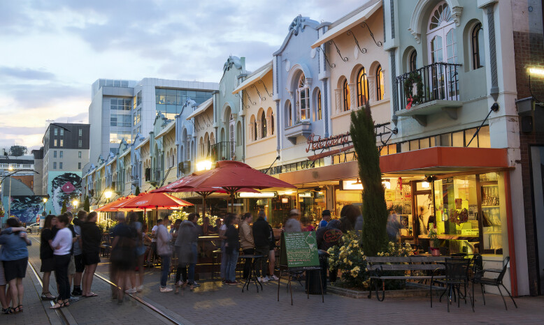 A street scene in the early evening with outdoor seating and red umbrellas