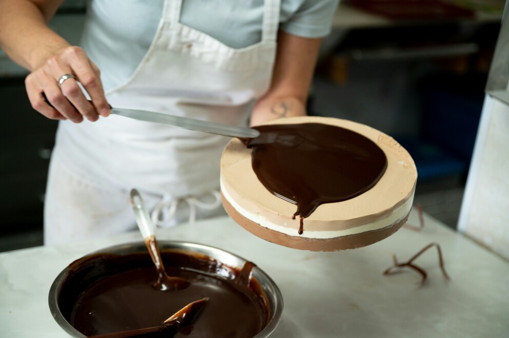 A photo of a person icing a cake with chocolate icing